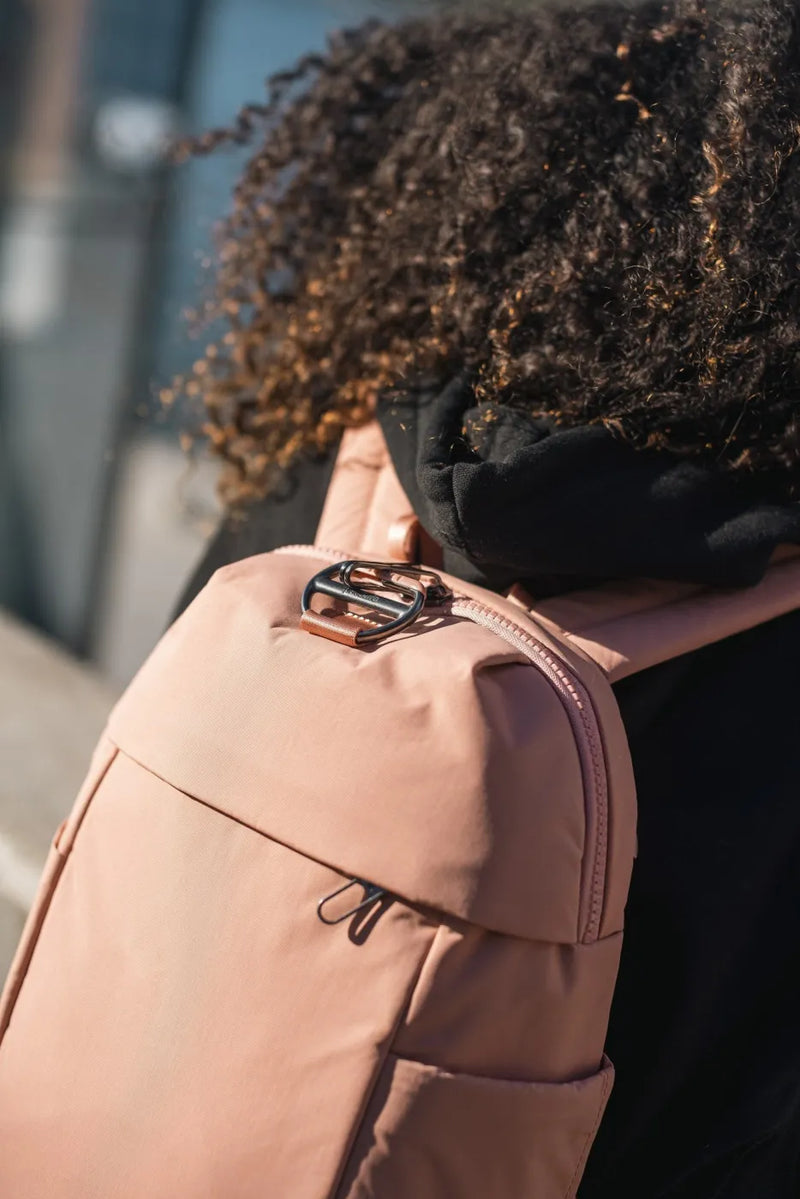 Pacsafe Citysafe CX Petite Anti-Theft 8L Backpack in Rose, worn on one shoulder with sunglasses hooked to the zip pull