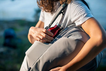 Pacsafe Eco 25L Anti-Theft 16" Laptop Backpack in Gravity Grey, a water bottle being slid into the side pocket