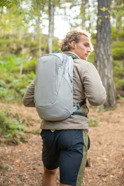 Pacsafe Eco 25L Anti-Theft 16" Laptop Backpack in Gravity Grey, worn on both shoulders by a man walking a woodland path
