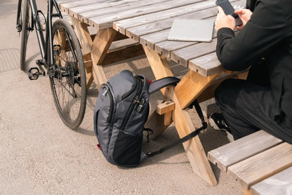 Pacsafe EXP Anti-Theft 28L 16" Laptop Backpack in Slate, propped against a picnic table beside a bicycle while its owner works