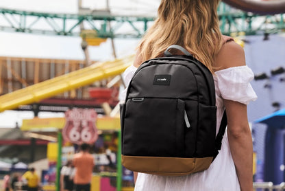 Pacsafe GO 15L Anti-Theft 13" Laptop Backpack in Jet Black, worn on both shoulders by a woman at a seaside funfair