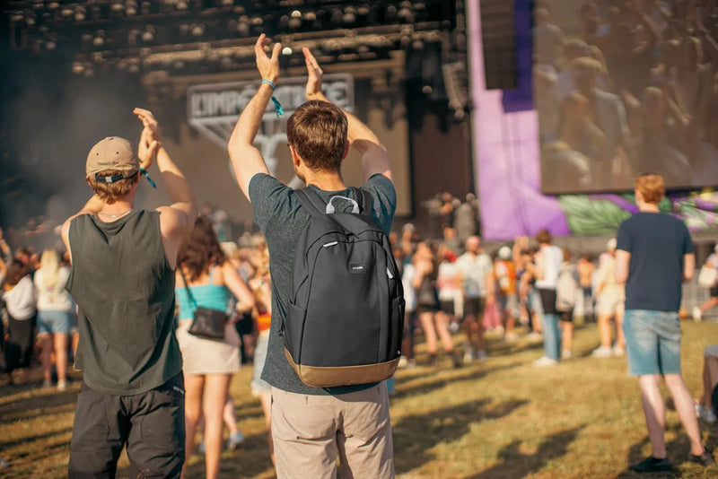 Pacsafe GO 25L Anti-Theft 16" Laptop Backpack in Jet Black, worn on both shoulders by a man in a festival crowd