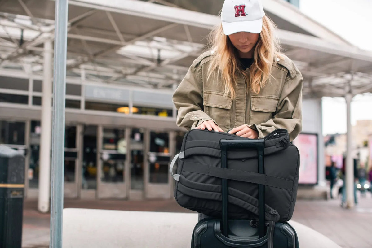 Pacsafe GO 34L Anti-Theft Carry-on Backpack in Jet Black, being packed on top of a cabin case outside a terminal