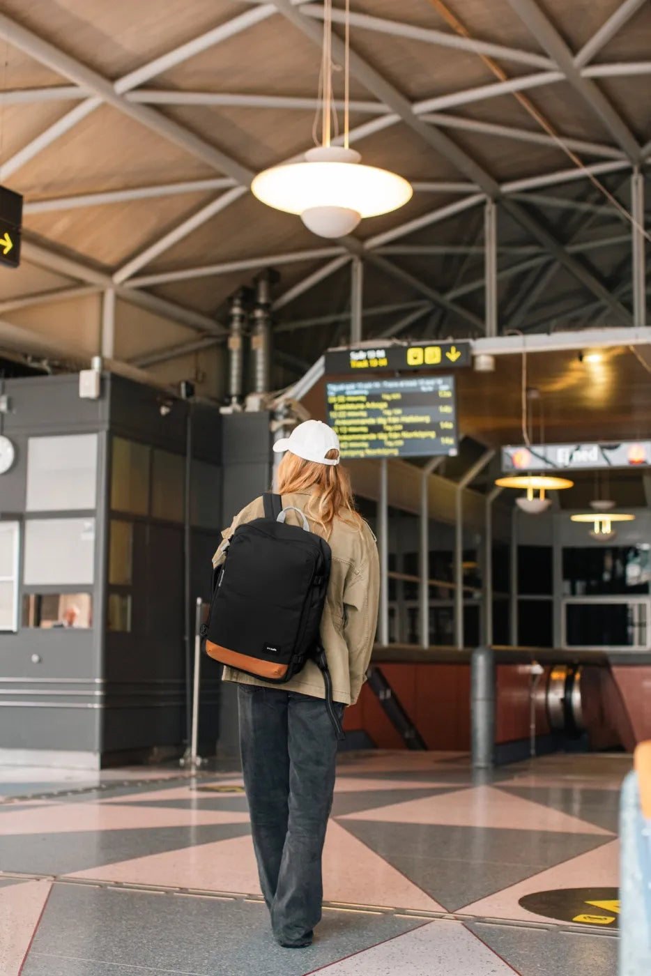 Pacsafe GO 34L Anti-Theft Carry-on Backpack in Jet Black, worn on both shoulders by a woman crossing a station concourse