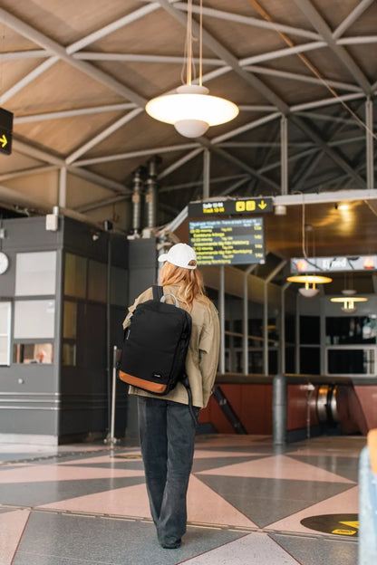 Pacsafe GO 34L Anti-Theft Carry-on Backpack in Jet Black, worn on both shoulders by a woman crossing a station concourse