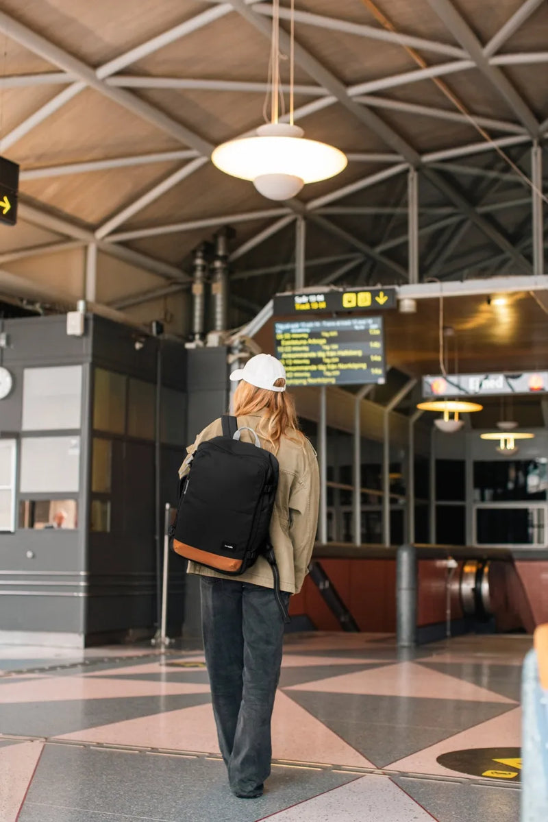 Pacsafe GO 34L Anti-Theft Carry-on Backpack in Jet Black, worn on both shoulders by a woman crossing a station concourse