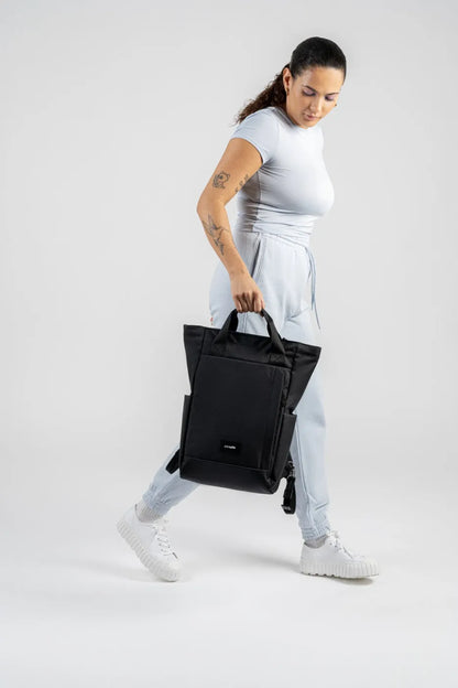 Pacsafe GO Anti-Theft 16" Laptop Totepack in Jet Black, carried by its top handles at the side of a woman walking