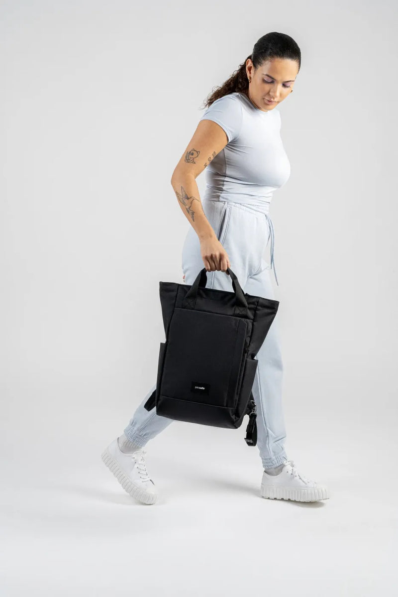 Pacsafe GO Anti-Theft 16" Laptop Totepack in Jet Black, carried by its top handles at the side of a woman walking