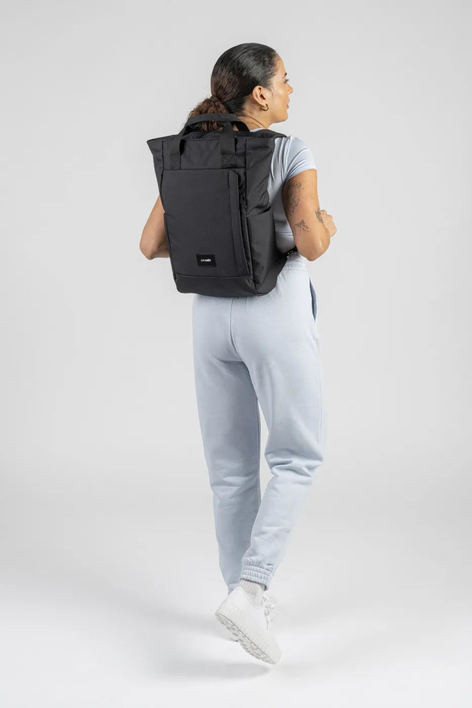 Pacsafe GO Anti-Theft 16" Laptop Totepack in Jet Black, worn as a backpack by a woman walking away from the camera
