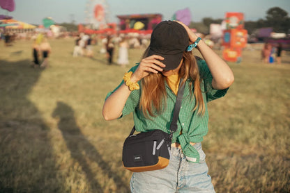 Pacsafe Go Anti-Theft Crossbody Bag in Jet Black, worn crossbody by a woman at a festival, adjusting her cap