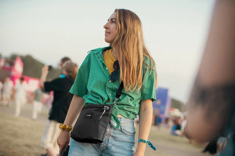 Pacsafe Go Anti-Theft Crossbody Pouch in Jet Black, worn crossbody by a woman walking through a festival field