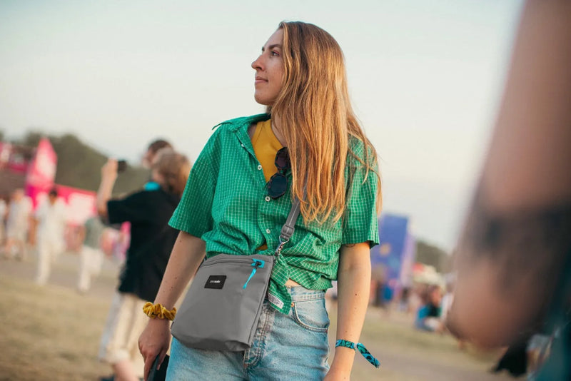Pacsafe Go Anti-Theft Crossbody Pouch in Stone, worn crossbody at the hip by a woman in a festival crowd
