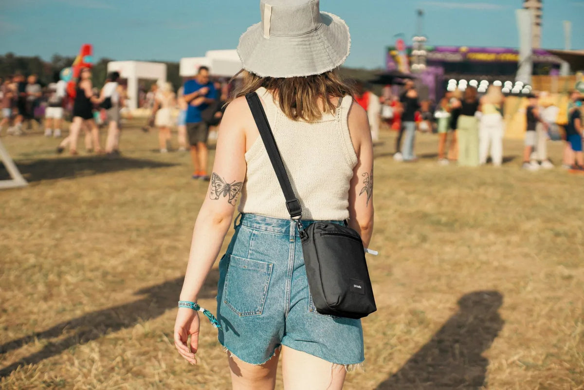 Pacsafe Go Anti-theft Festival Crossbody Bag in Jet Black, worn crossbody at the hip by a woman walking through a festival field