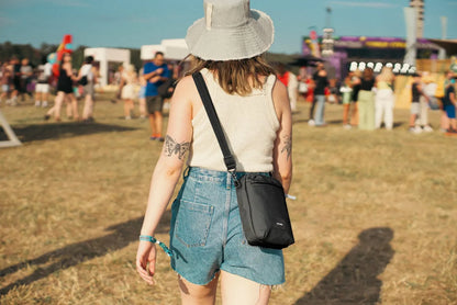 Pacsafe Go Anti-theft Festival Crossbody Bag in Jet Black, worn crossbody at the hip by a woman walking through a festival field