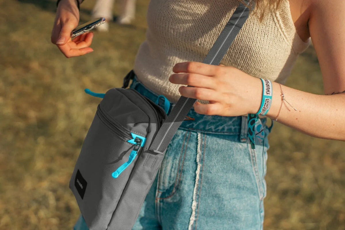 Pacsafe Go Anti-theft Festival Crossbody Bag in Stone, worn crossbody at the hip while a phone is taken from the front pocket
