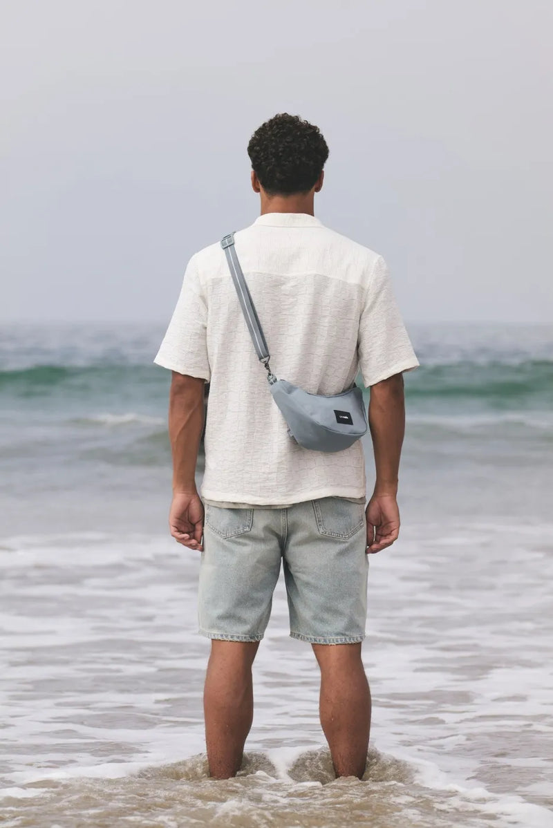 Pacsafe Go Anti-Theft Lunar Crossbody Bag in Fresh Mint, worn crossbody by a man standing in the shallows, seen from behind