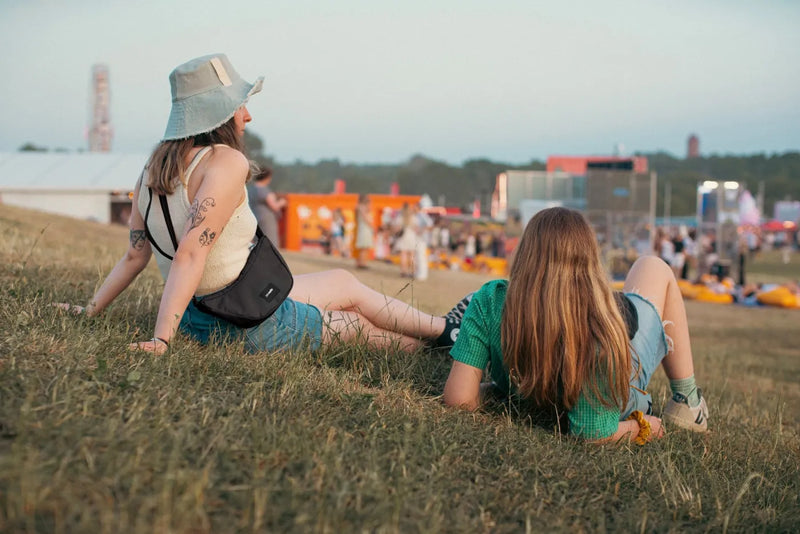 Pacsafe Go Anti-Theft Lunar Crossbody Bag in Jet Black, worn crossbody by a woman sitting on the grass at a festival