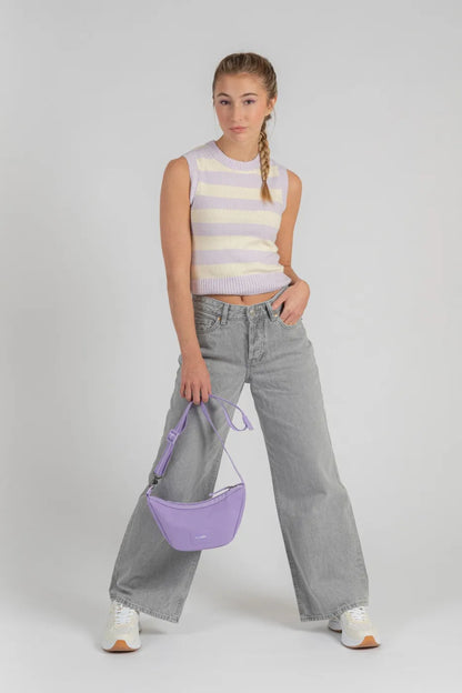 Pacsafe Go Anti-Theft Lunar Crossbody Bag in Lavender, held by its long strap beside a woman in a striped knit and grey jeans