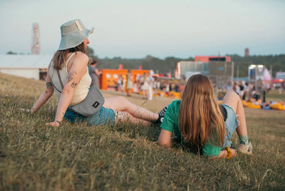 Pacsafe Go Anti-Theft Lunar Crossbody Bag in Stone, worn crossbody by a woman sitting on the grass at an outdoor festival