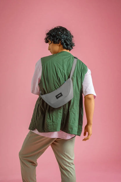 Pacsafe Go Anti-Theft Lunar Crossbody Bag in Stone, worn crossbody at the hip by a man in a green vest, seen from behind