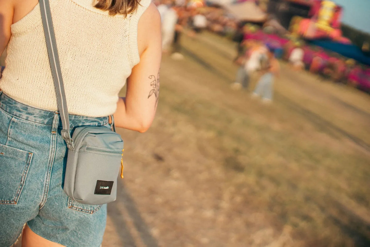 Pacsafe Go Anti-theft Micro Crossbody Bag in Fresh Mint, worn crossbody at the hip by a woman walking a festival field