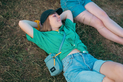 Pacsafe Go Anti-theft Micro Crossbody Bag in Fresh Mint, worn crossbody by a woman lying back on the grass