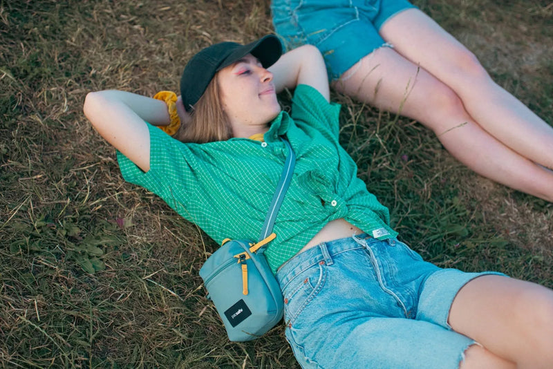Pacsafe Go Anti-theft Micro Crossbody Bag in Fresh Mint, worn crossbody by a woman lying back on the grass