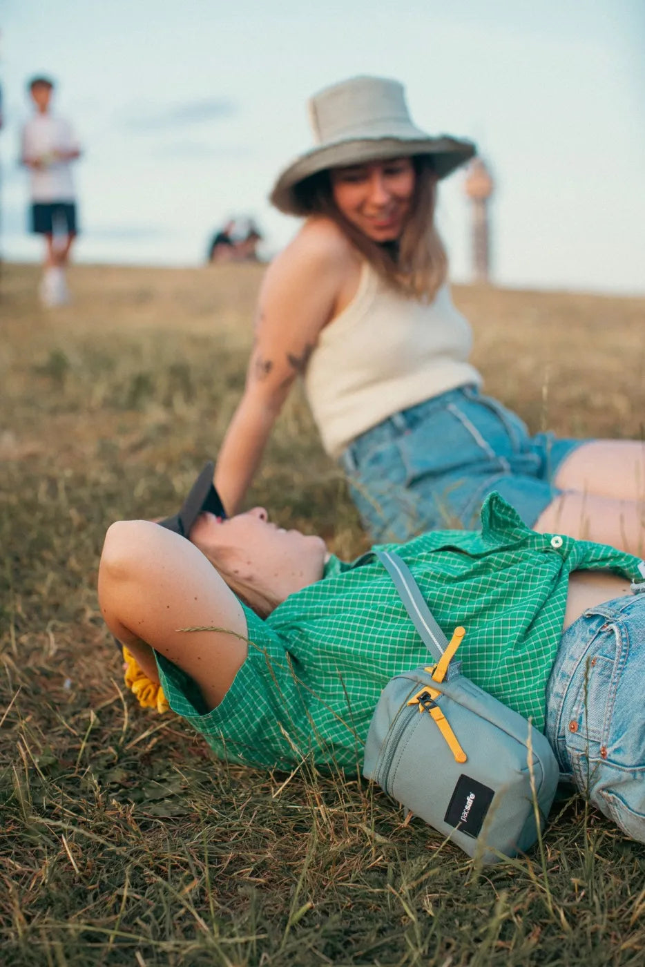 Pacsafe Go Anti-theft Micro Crossbody Bag in Fresh Mint, worn at the waist by a woman lying on the grass at a festival