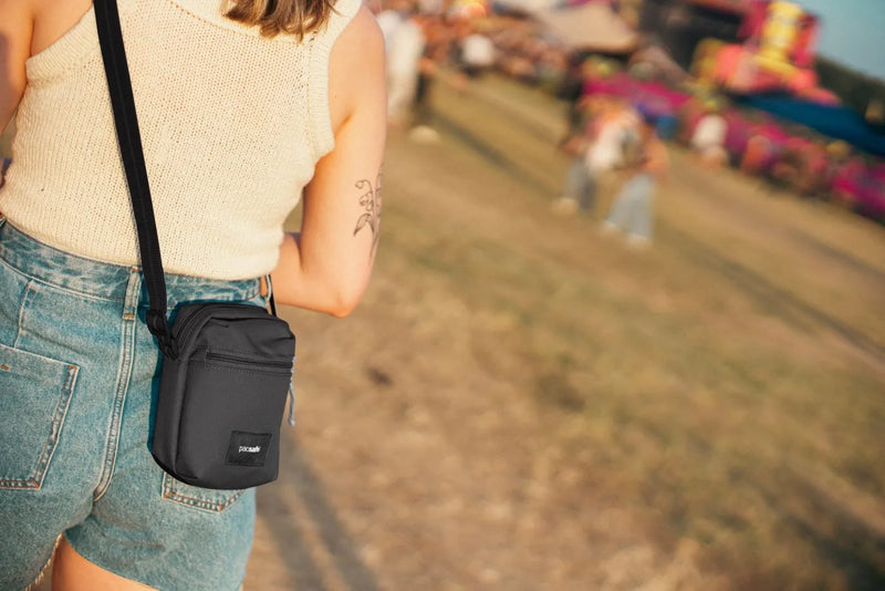 Pacsafe Go Anti-theft Micro Crossbody Bag in Jet Black, worn crossbody at the hip over denim shorts at a festival