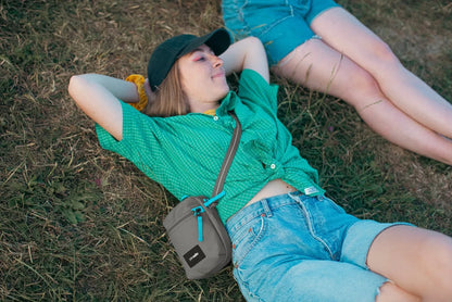 Pacsafe Go Anti-theft Micro Crossbody Bag in Stone, worn crossbody by a woman lying on the grass at a festival