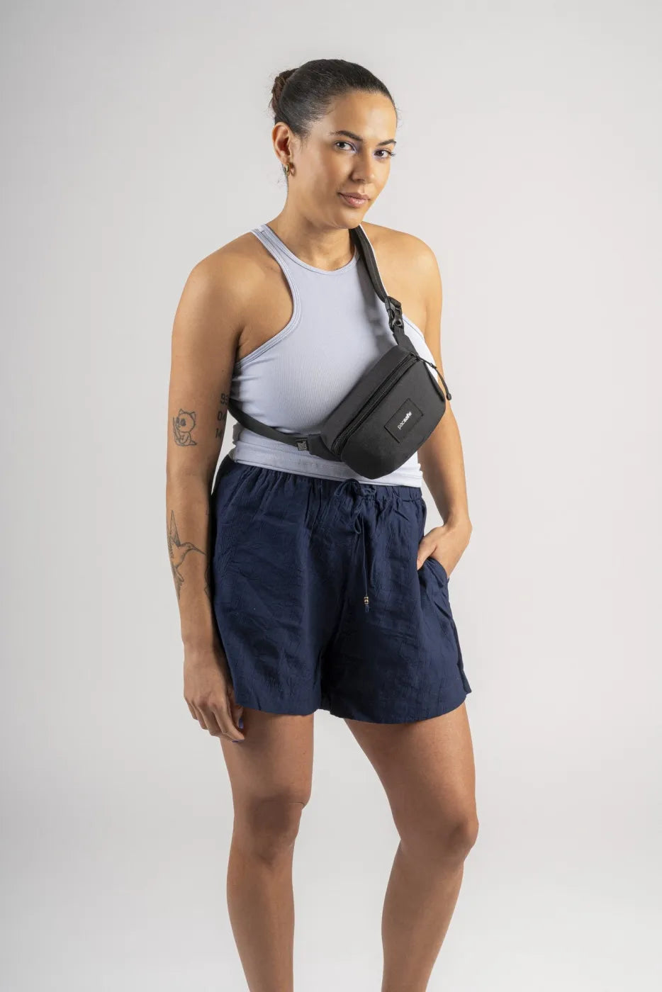 Pacsafe Go Anti-Theft Micro Sling in Jet Black, worn across the chest over a white tank top and shorts