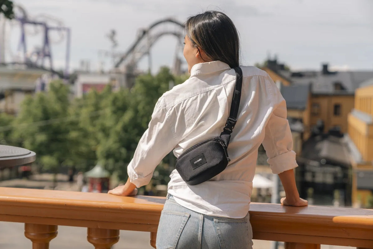 Pacsafe Go Anti-Theft Micro Sling in Jet Black, worn crossbody at the back by a woman looking out over a funfair