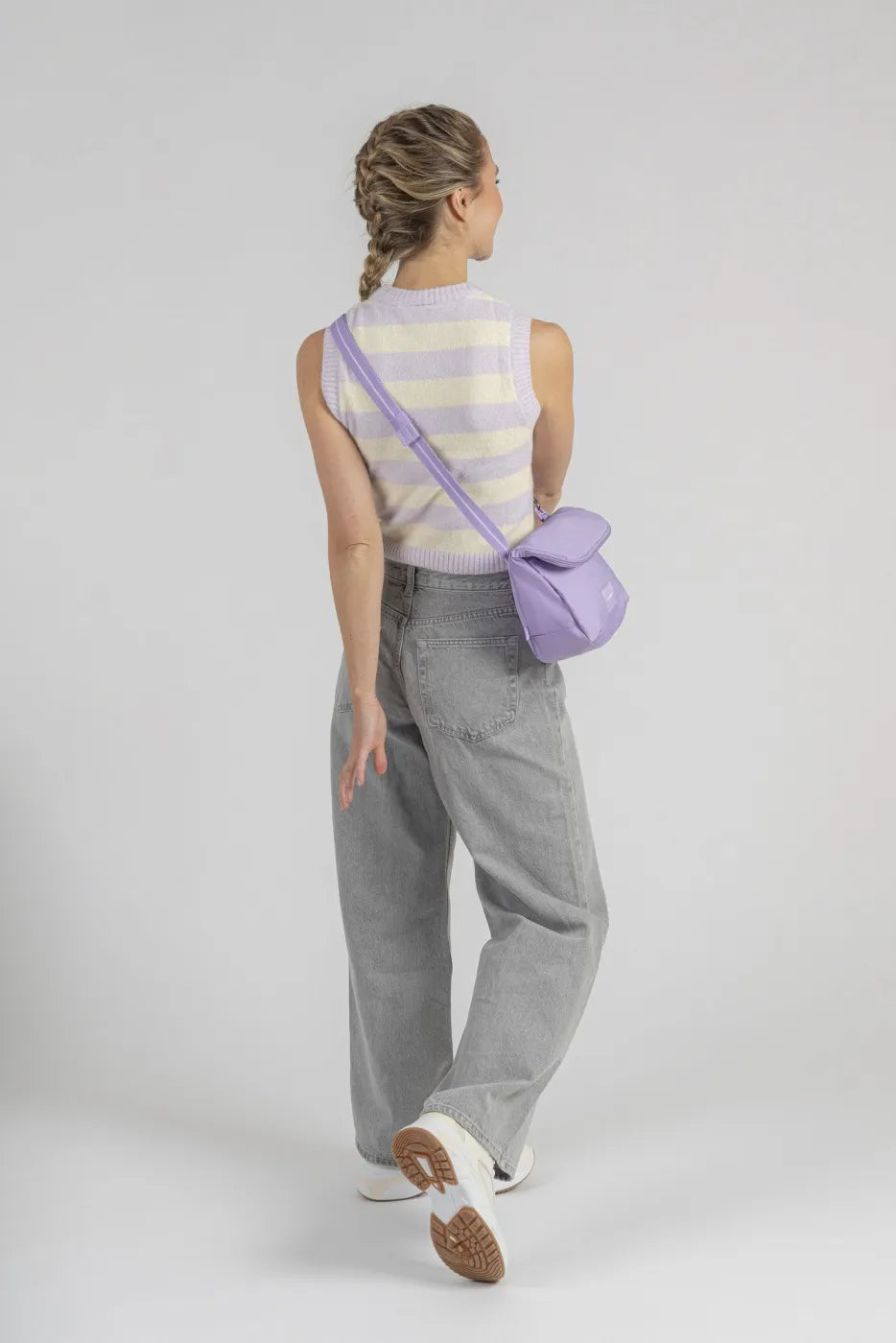 Pacsafe Go Anti-Theft Saddle Crossbody Bag in Lavender, worn crossbody at the back of a woman in grey jeans, seen from behind
