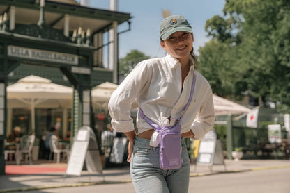 Pacsafe Go Anti-Theft Tech Crossbody Bag in Lavender, worn crossbody at the hip by a woman outside a garden restaurant
