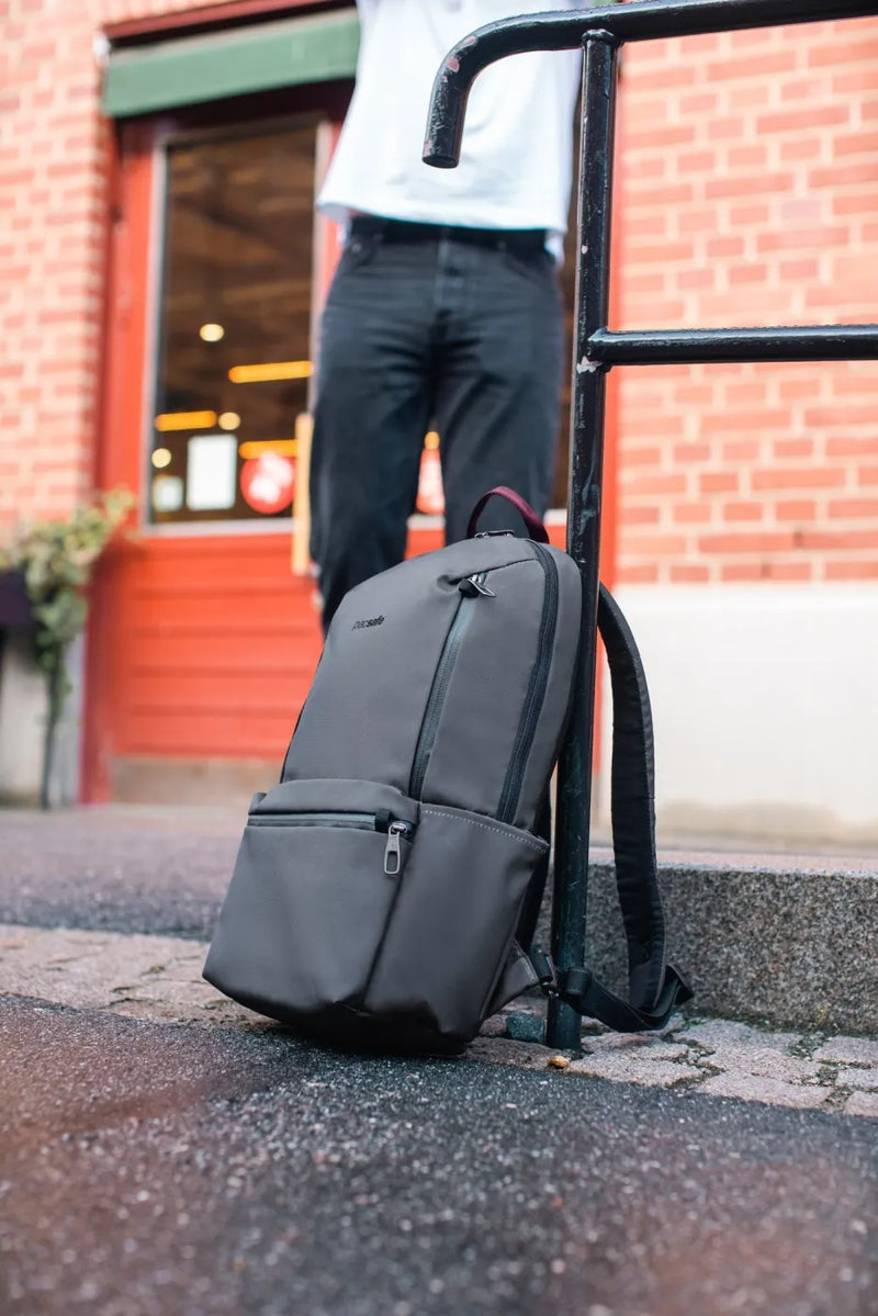 Pacsafe Metrosafe X Anti-Theft 20L 16" Laptop Backpack in Slate, locked to a railing outside a red shopfront