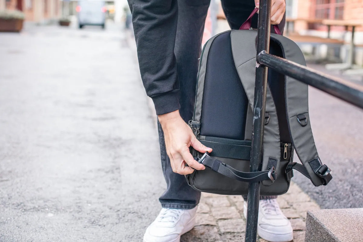 Pacsafe Metrosafe X Anti-Theft 20L 16" Laptop Backpack in Slate, the strap being clipped to a railing on a cobbled street