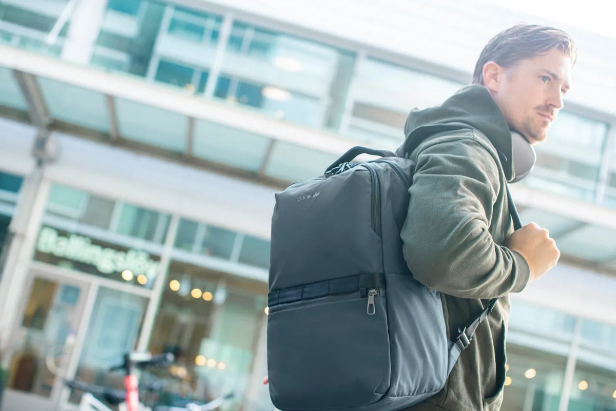 Pacsafe Metrosafe X Anti-Theft 25L 16" Laptop Backpack in Slate, worn on both shoulders by a man walking past a shopfront
