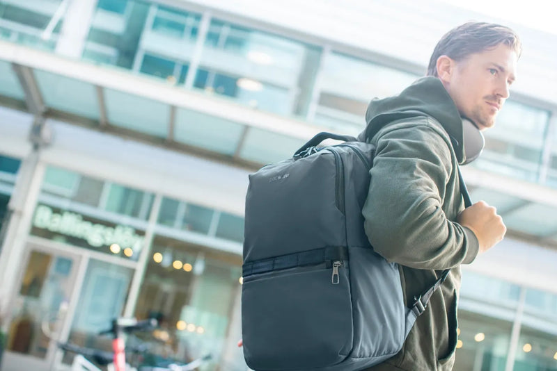Pacsafe Metrosafe X Anti-Theft 25L 16" Laptop Backpack in Slate, worn on both shoulders by a man walking past a shopfront