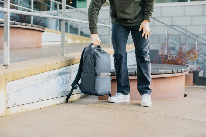 Pacsafe Metrosafe X Anti-Theft 25L 16" Laptop Backpack in Slate, set down on a walkway beside a man in jeans