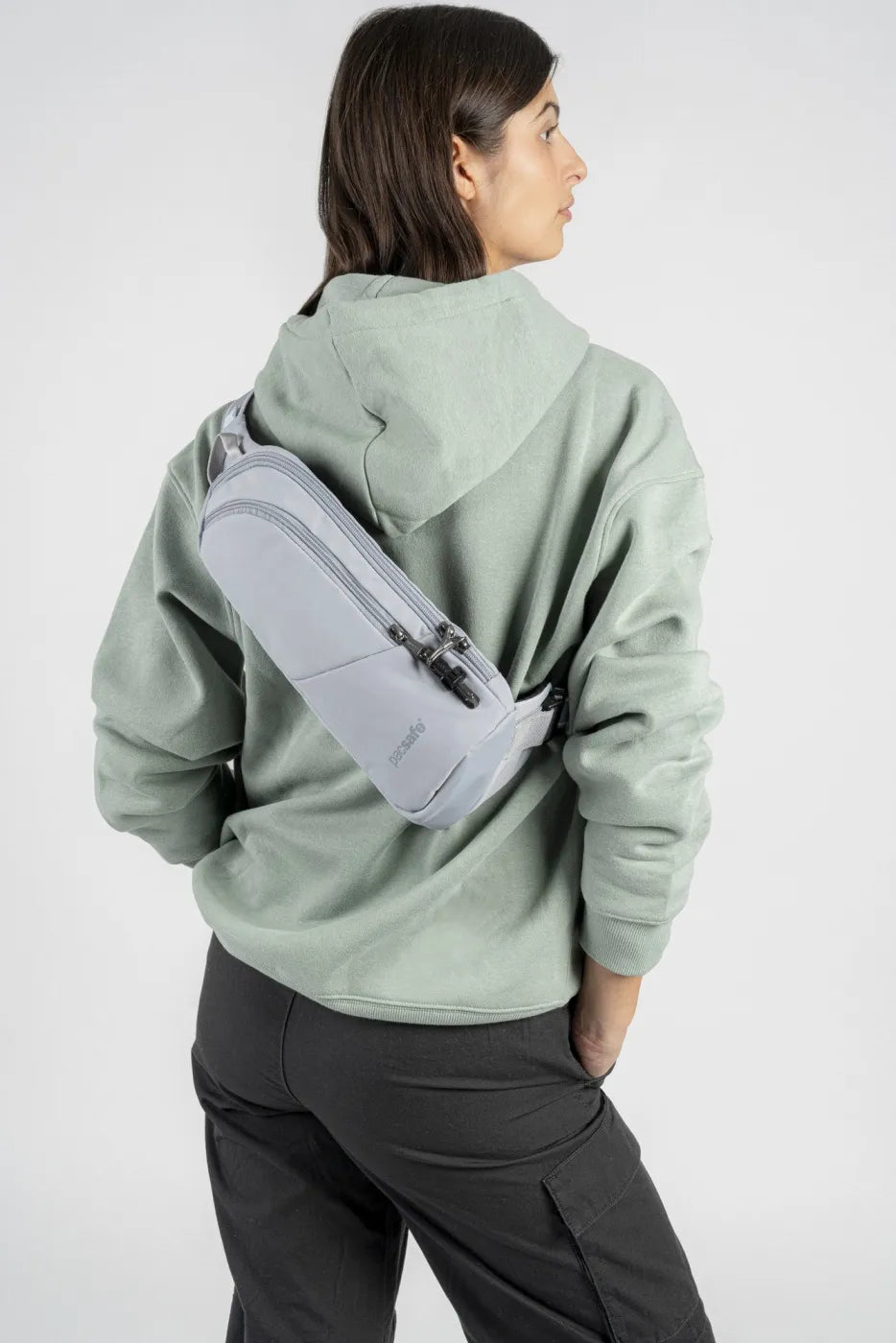 Pacsafe V Action Anti-Theft Sling Pack in Digital Grey, worn across the back of a woman in a green hoodie, seen from behind