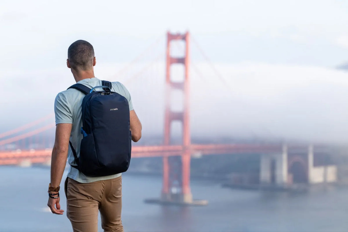 Pacsafe V Active 24L Anti-Theft 13" Laptop Backpack in Ocean, worn on both shoulders by a man looking out at the Golden Gate Bridge