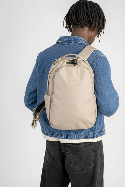 Pacsafe V All-Around 16L Anti-Theft 13" Laptop Backpack in Beige, worn on both shoulders over a denim jacket, seen from behind
