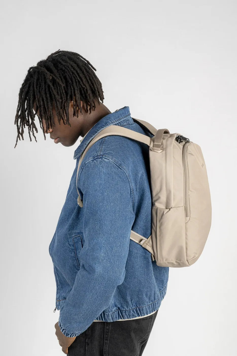 Pacsafe V All-Around 16L Anti-Theft 13" Laptop Backpack in Beige, worn on both shoulders over a denim jacket, seen from the side