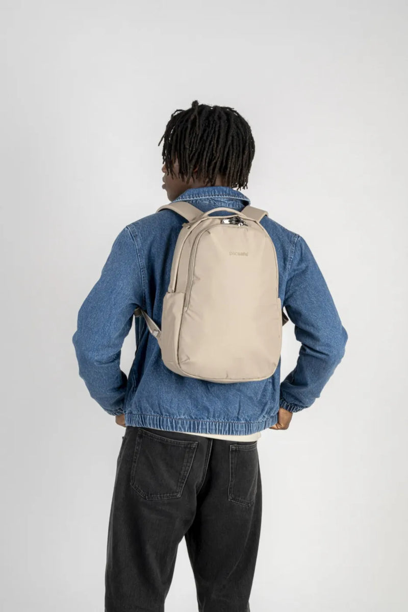 Pacsafe V All-Around 16L Anti-Theft 13" Laptop Backpack in Beige, worn on both shoulders over a denim jacket, seen from behind