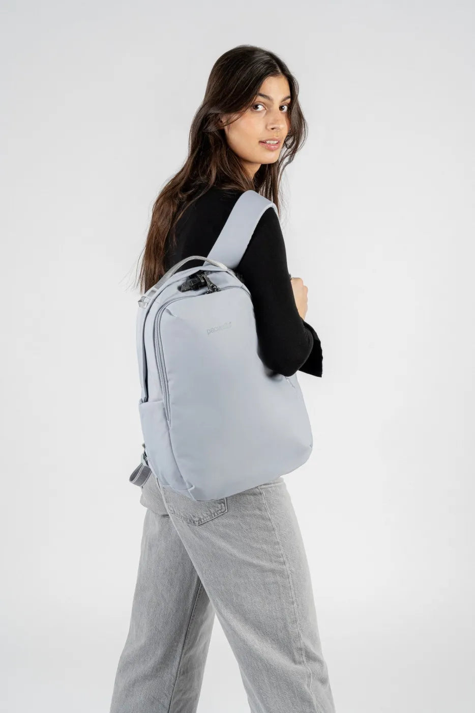 Pacsafe V All-Around 16L Anti-Theft 13" Laptop Backpack in Digital Grey, worn on both shoulders by a woman looking back over her shoulder