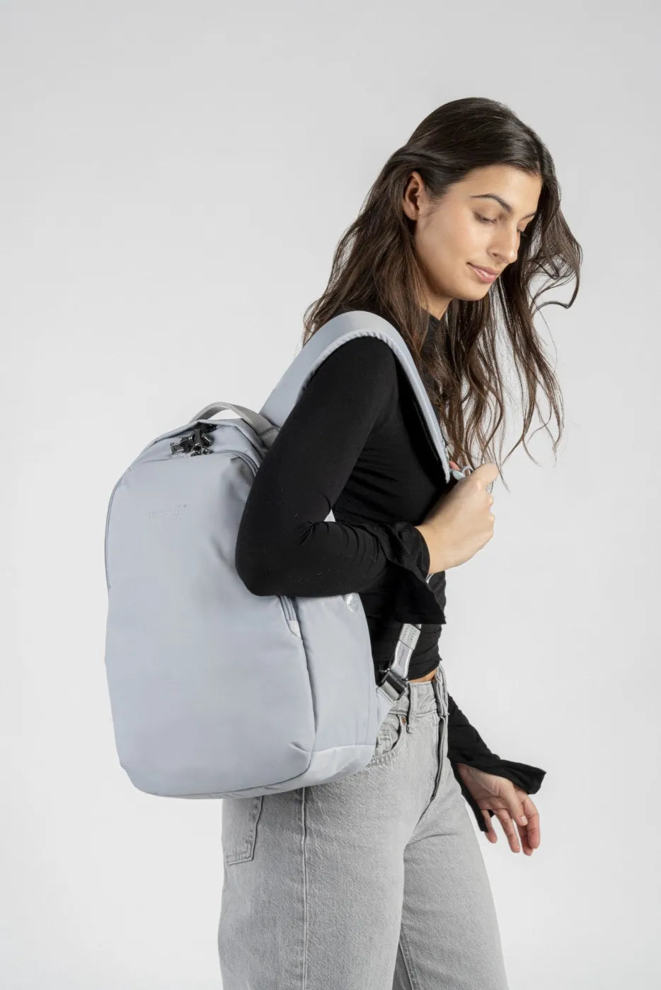 Pacsafe V All-Around 16L Anti-Theft 13" Laptop Backpack in Digital Grey, swung onto one shoulder by a woman in a black top