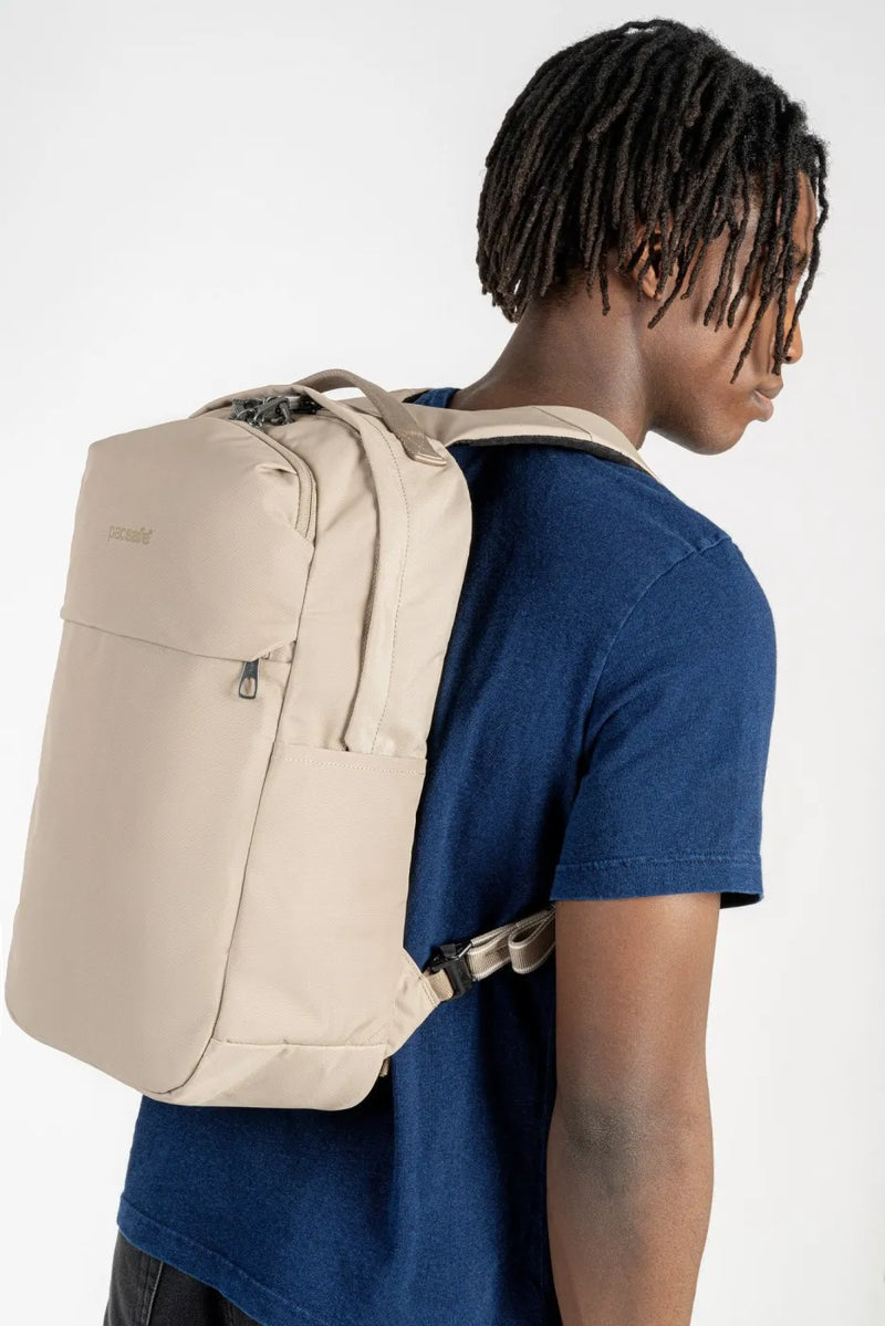 Pacsafe V City 20L Anti-Theft 16" Laptop Backpack in Beige, worn on both shoulders by a man in a navy tee, seen from the side