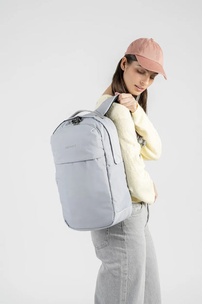 Pacsafe V City 20L Anti-Theft 16" Laptop Backpack in Digital Grey, held over one shoulder by a woman in a pink cap and yellow knit