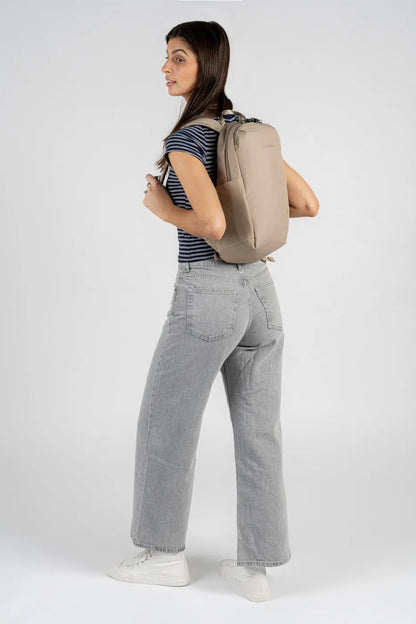 Pacsafe V Tech 12L Anti-Theft Backpack in Beige, worn on both shoulders by a woman in grey jeans, seen from behind