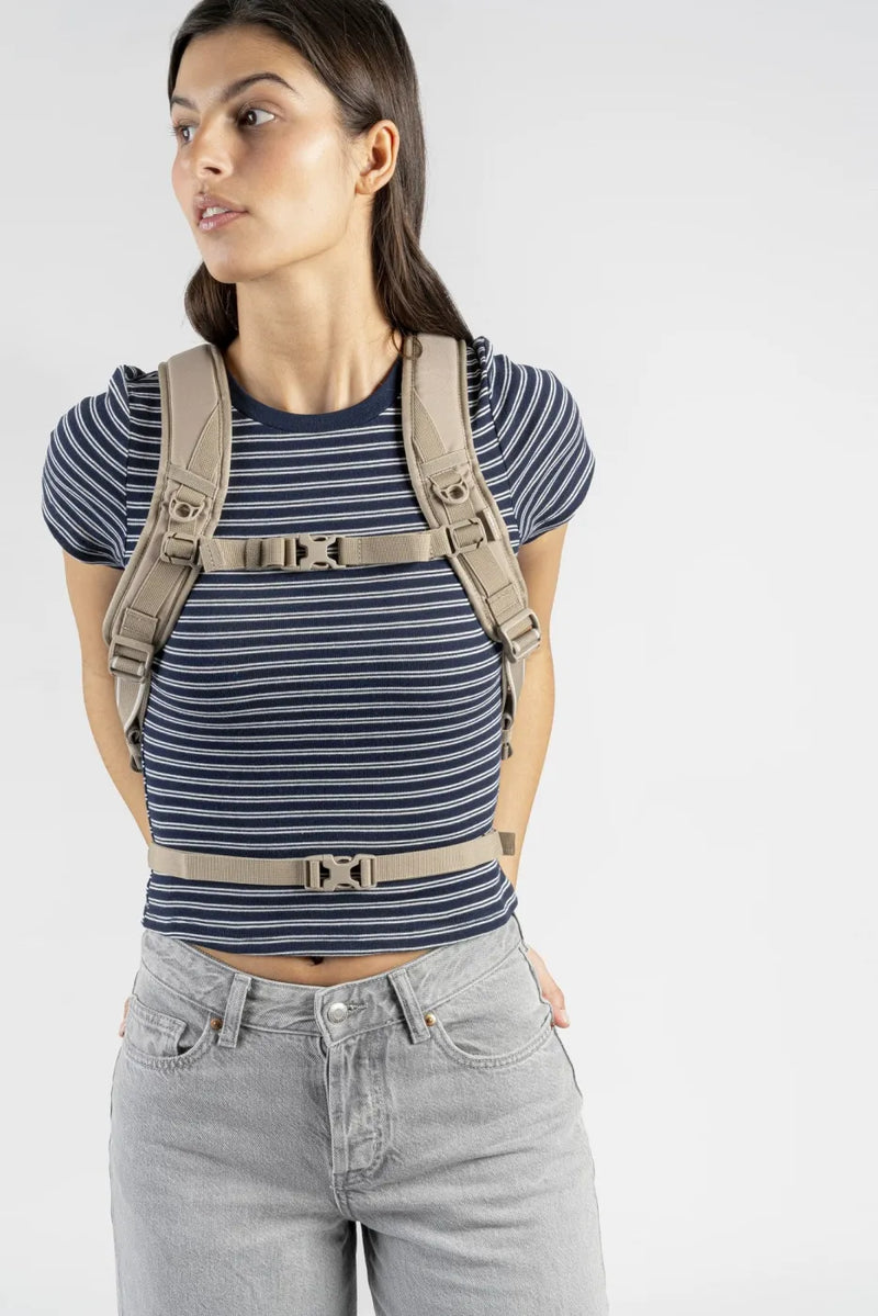 Pacsafe V Tech 12L Anti-Theft Backpack in Beige, chest and waist straps clipped over a striped tee, seen from the front